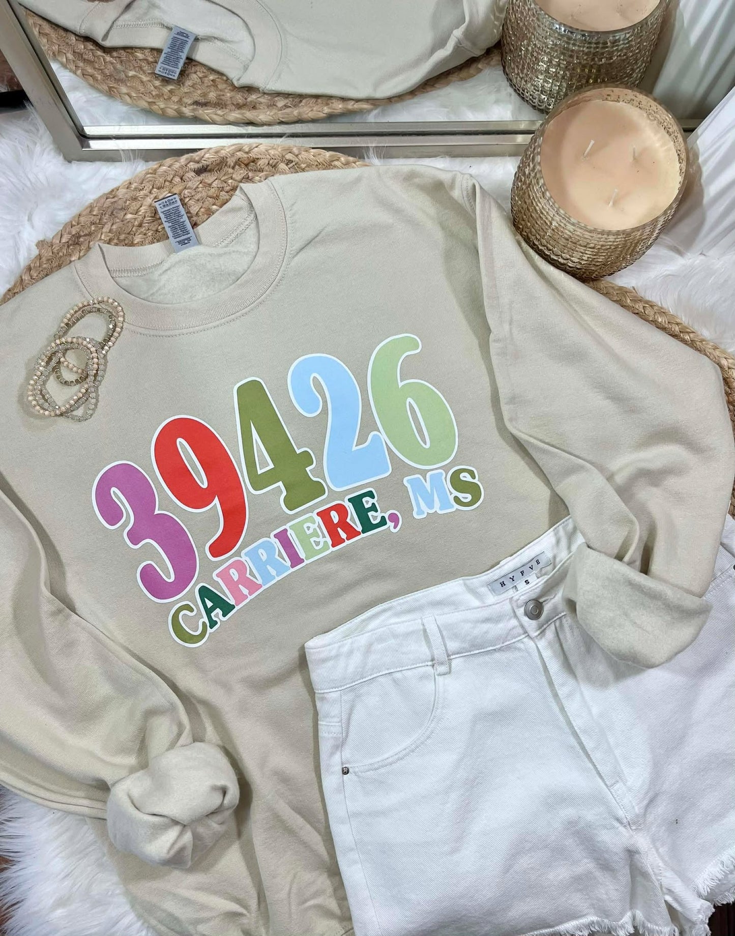 Beige sweatshirt with colorful zipcode text on a bed