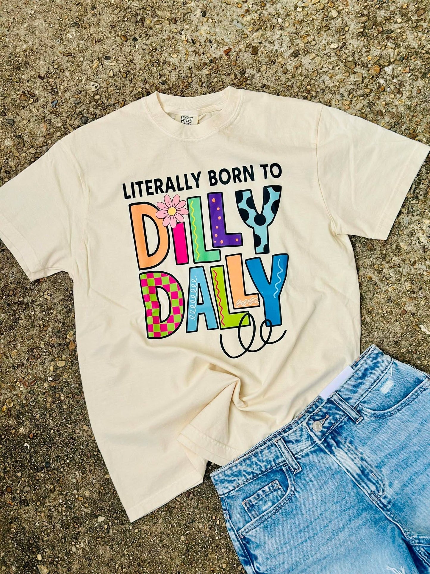 Beige t-shirt with colorful text 'Dilly Dally' on a textured surface