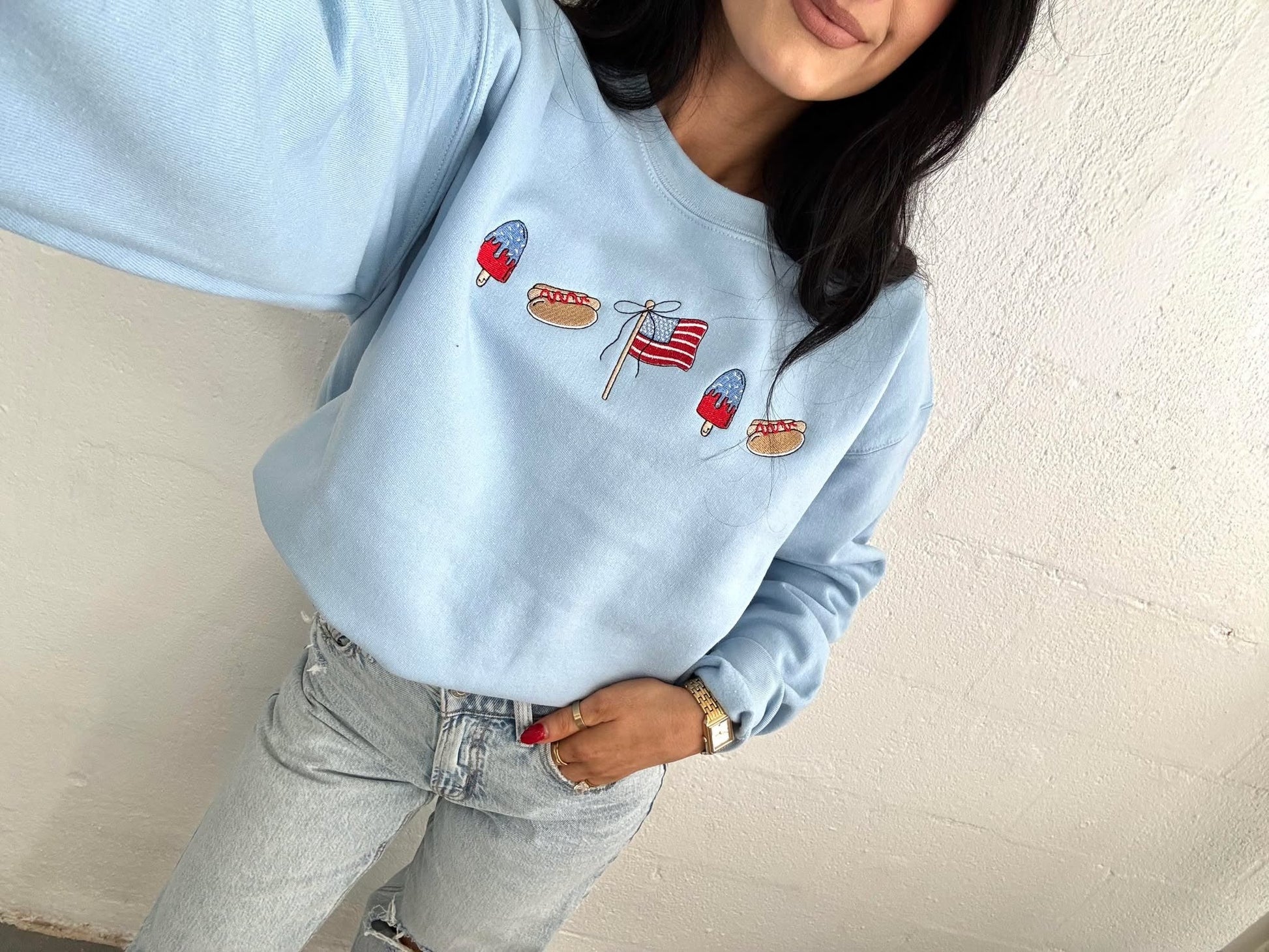 Person wearing a light blue sweatshirt with embroidered designs against a plain background