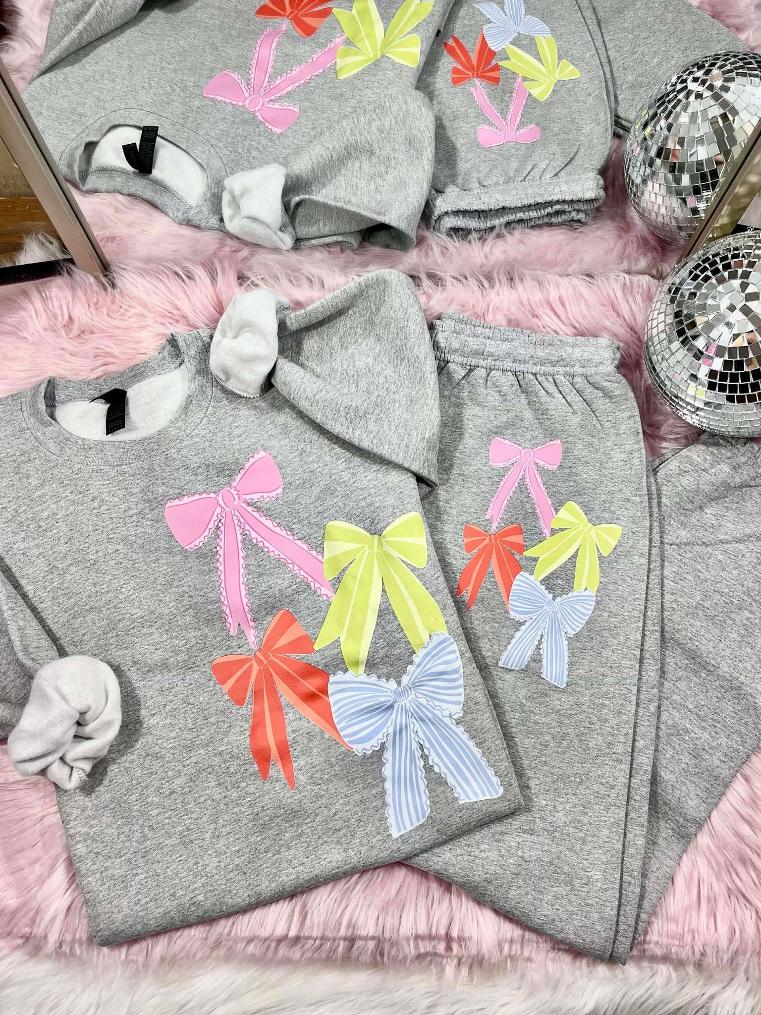 Gray sweatshirt and pants set with colorful bows on a pink surface.